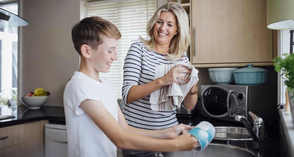 Mother and teenage son laughing as they wash up together in the kitchen