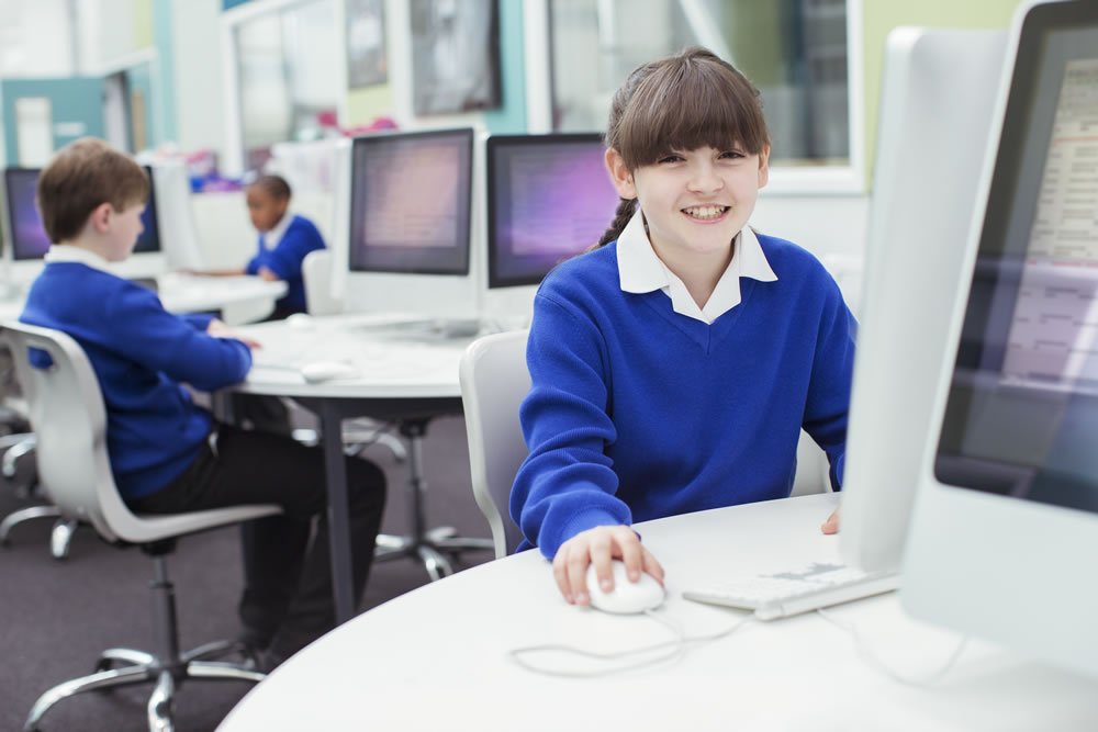 Smiling pupil in a blue school jumper using a computer in a school IT room