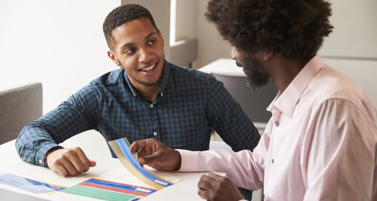Young man smiling as an adviser points to a colourful leaflet on the table between them