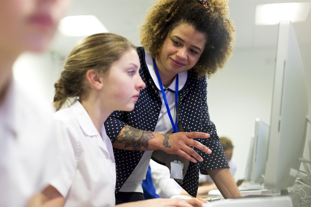 Teacher helping a pupil at a computer in a school IT room