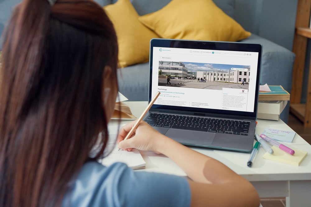 Student viewing a university course profile for Psychology on a laptop while taking notes