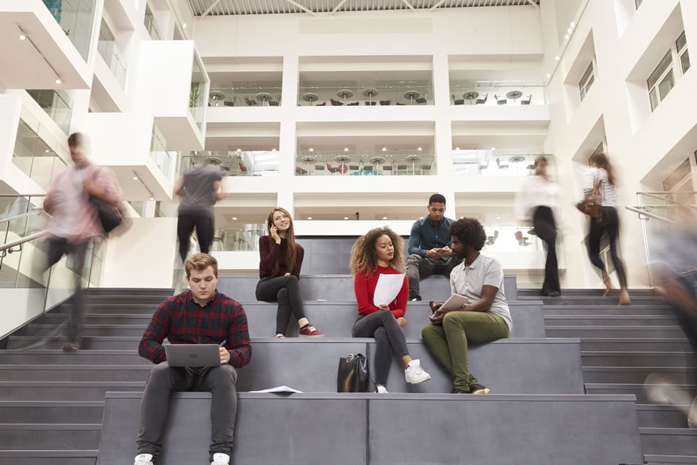 Students sitting and walking on wide steps in a modern university atrium