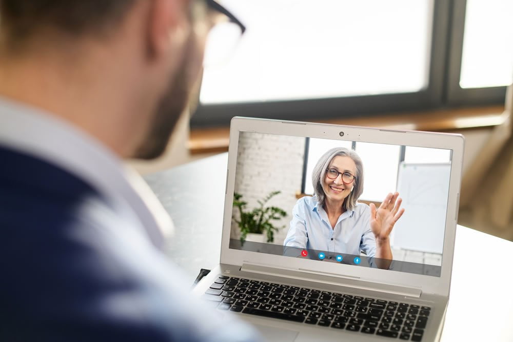 Man on a video call with a smiling woman waving on his laptop screen